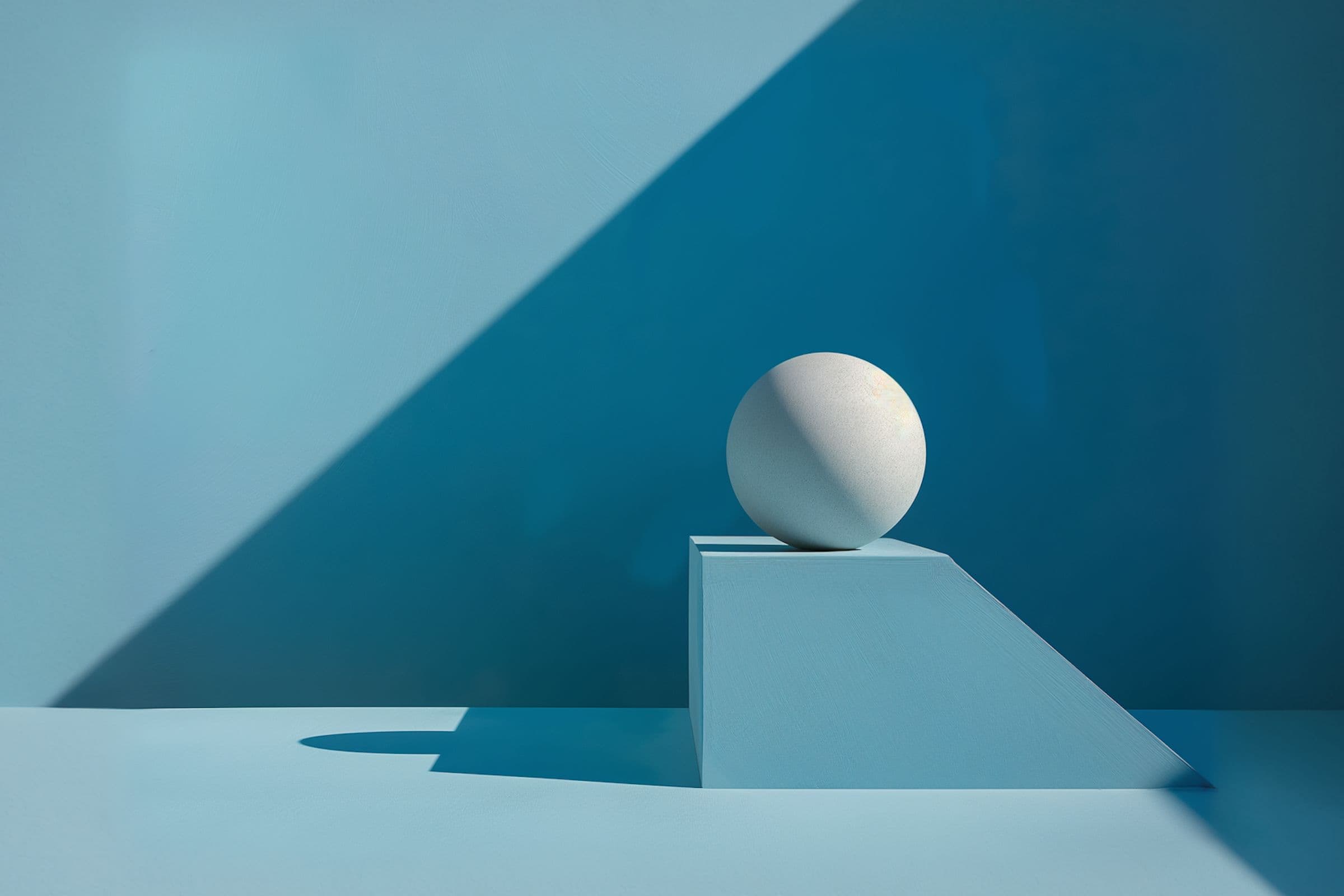 A white sphere on a blue geometric pedestal casts a shadow, with a diagonal light creating contrasting shapes on a blue background.
